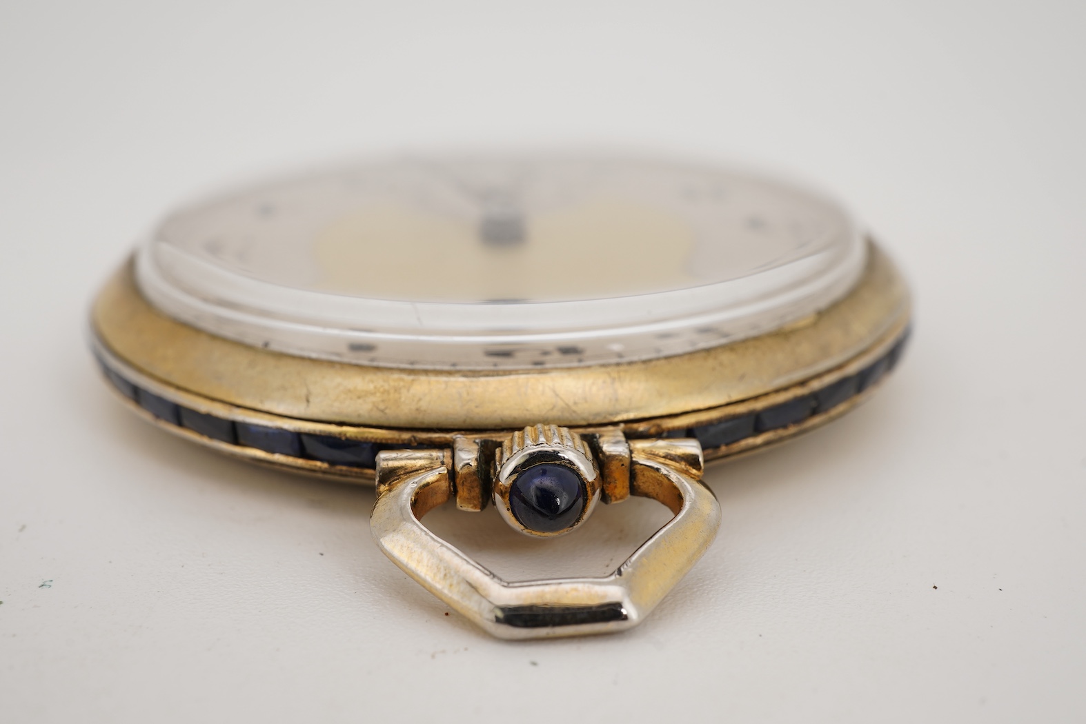 A French Art Deco parcel gilt white metal open faced dress pocket watch, with synthetic sapphire set border and winding crown